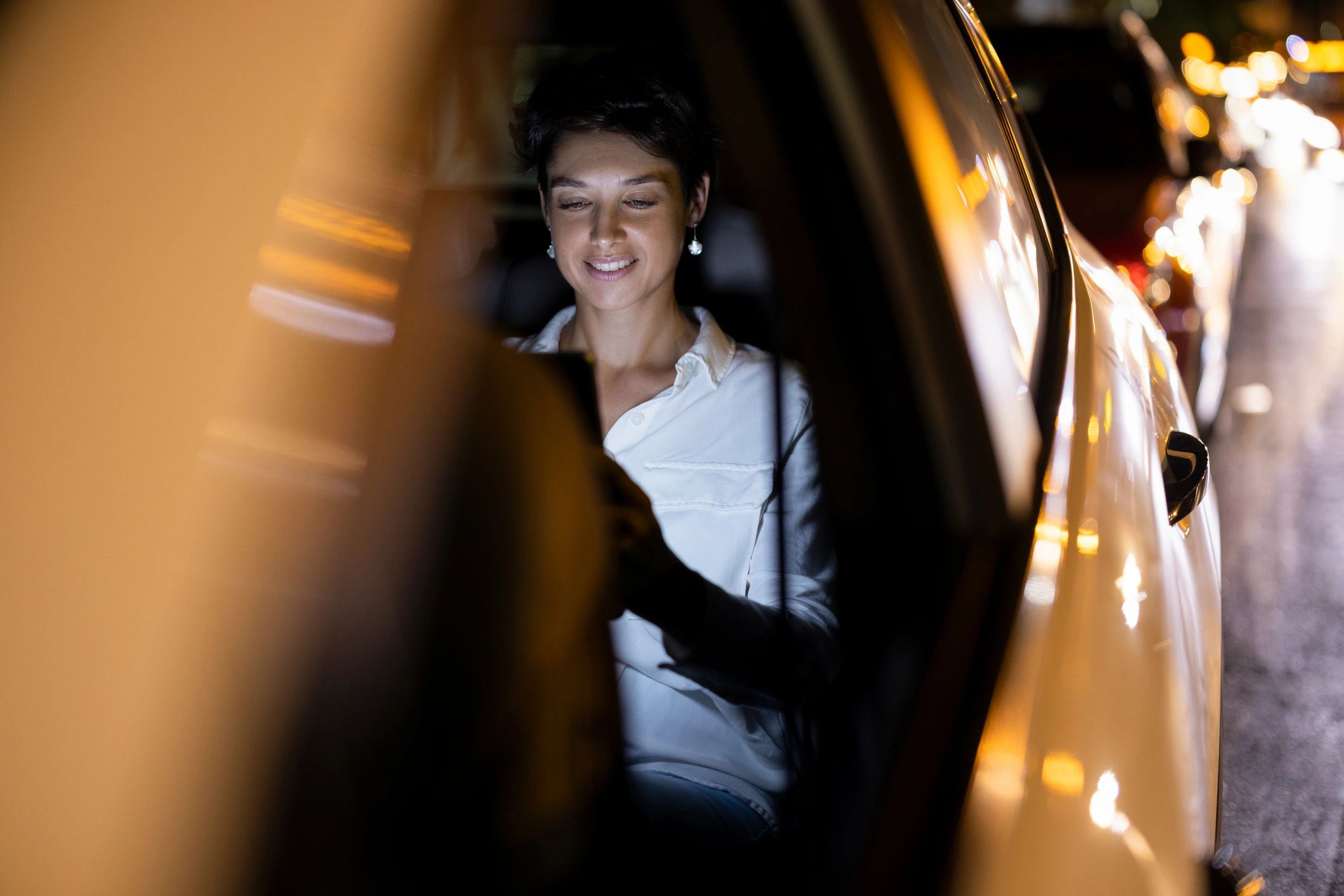 Woman using a tablet in a car at night with city lights